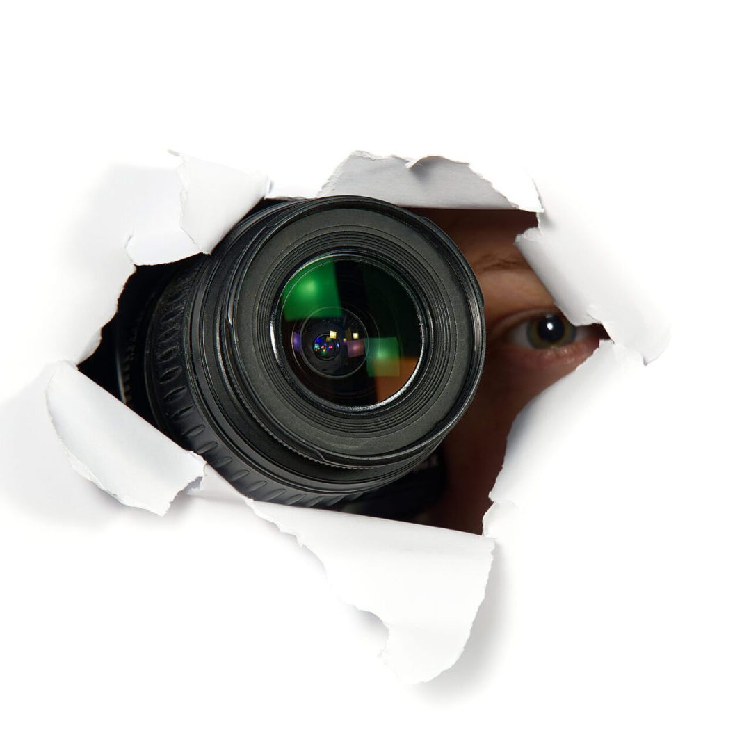 A camera peeking through ripped paper