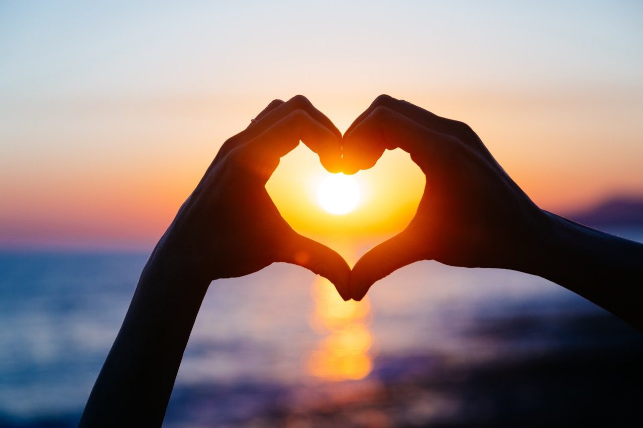 A person forming a heart with their hands showing the sun